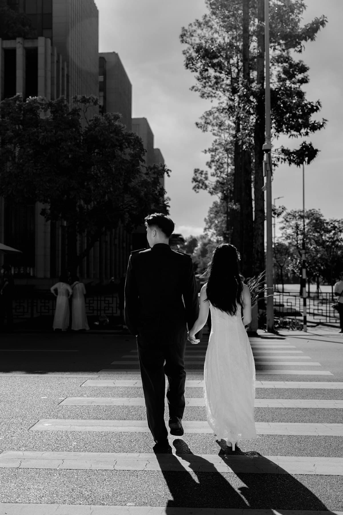 Đôi trẻ nắm tay qua đường ở Hà Nội, bóng đổ dài trên vạch kẻ