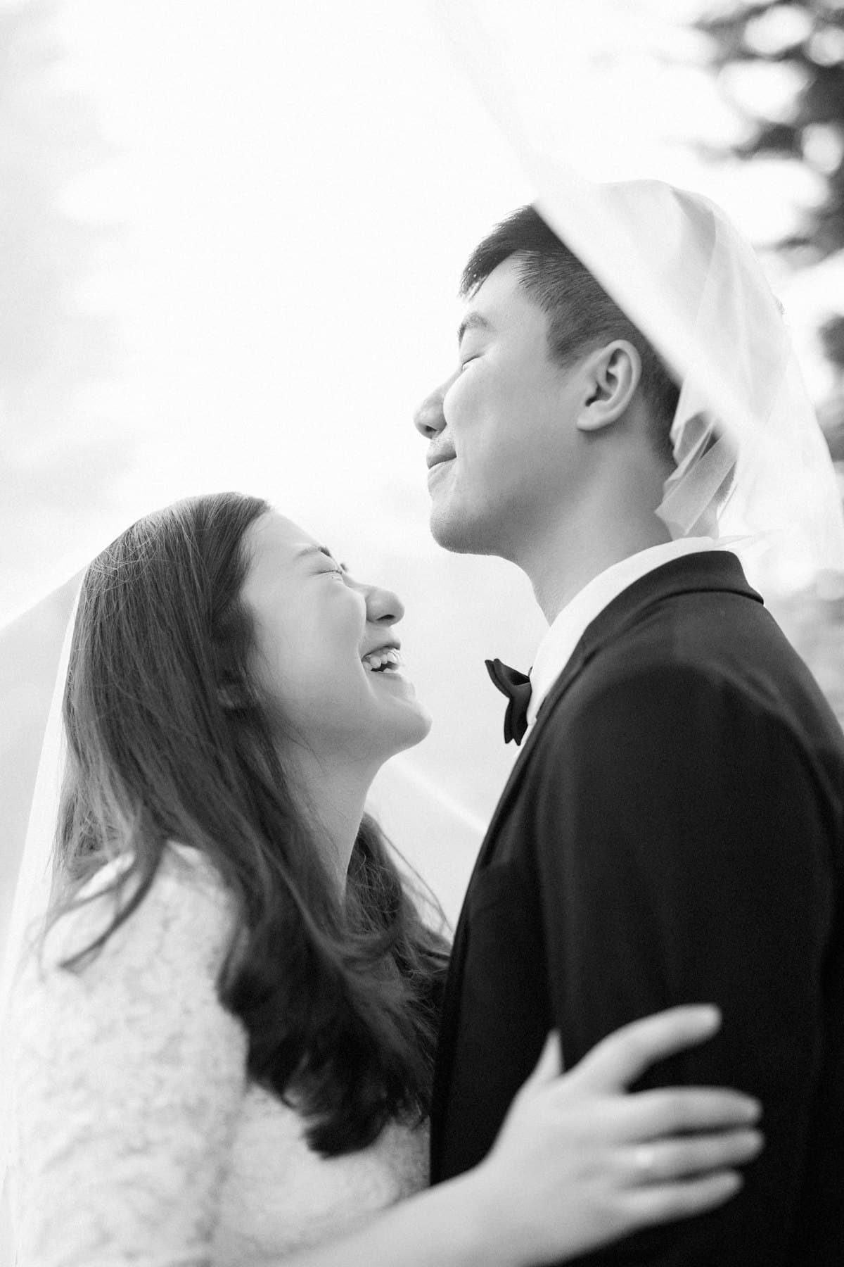 Cô dâu và chú rể cười với nhau dưới tấm voan