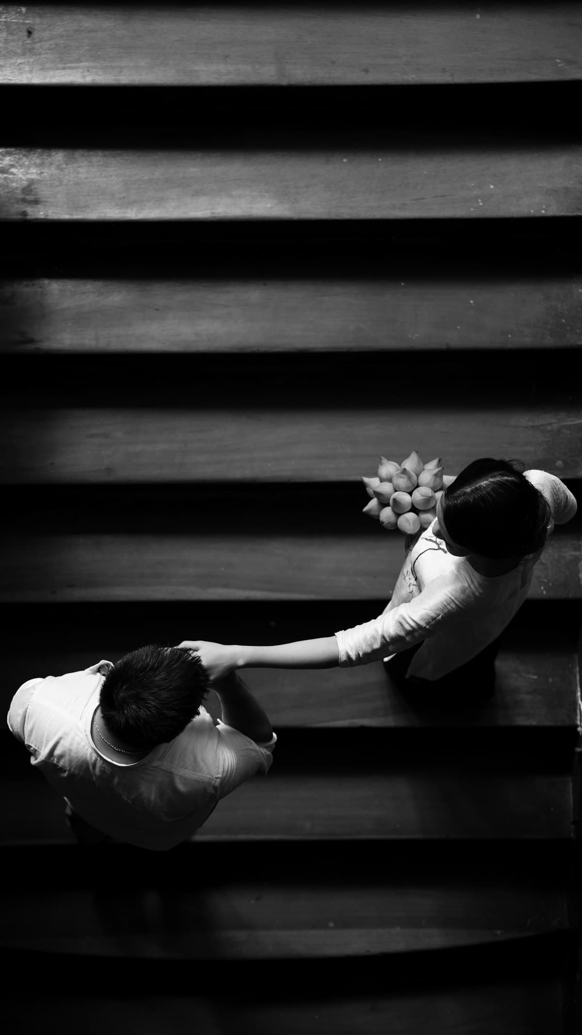 Nhìn từ trên xuống: cô gái cầm hoa dắt tay chàng trai trên bậc cầu thang